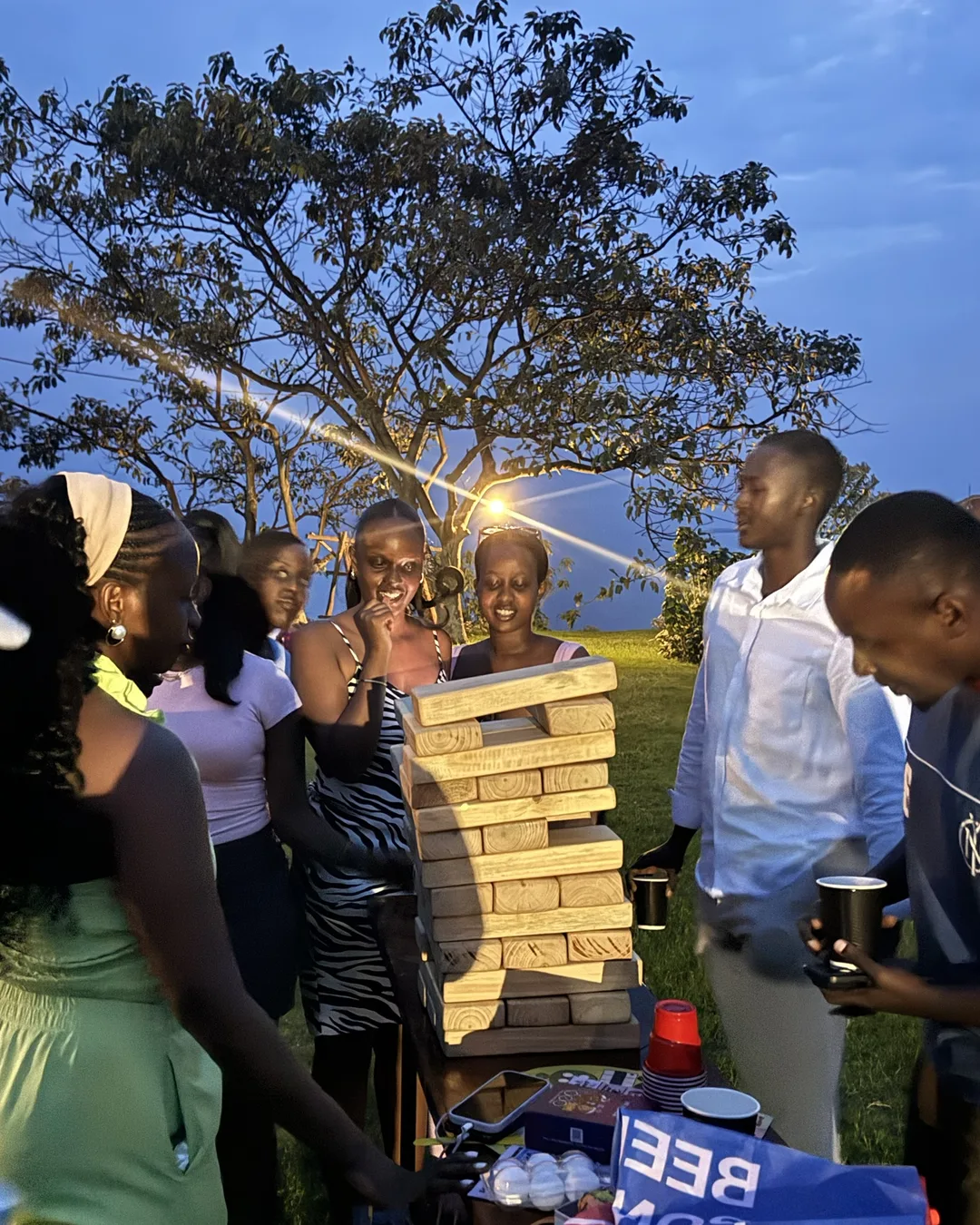 Friends laughing around Giant Jenga at dusk